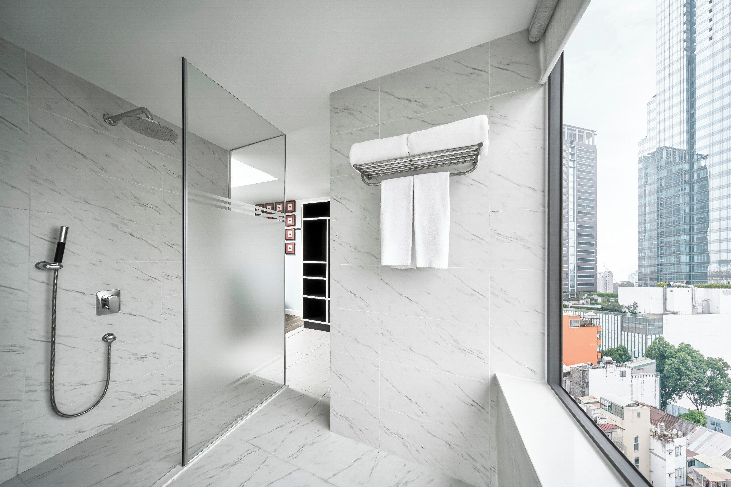 Ein modernes Badezimmer mit Duschkabine aus Glas, Handtuchhalter und Blick auf die Stadt durch ein großes Fenster.
