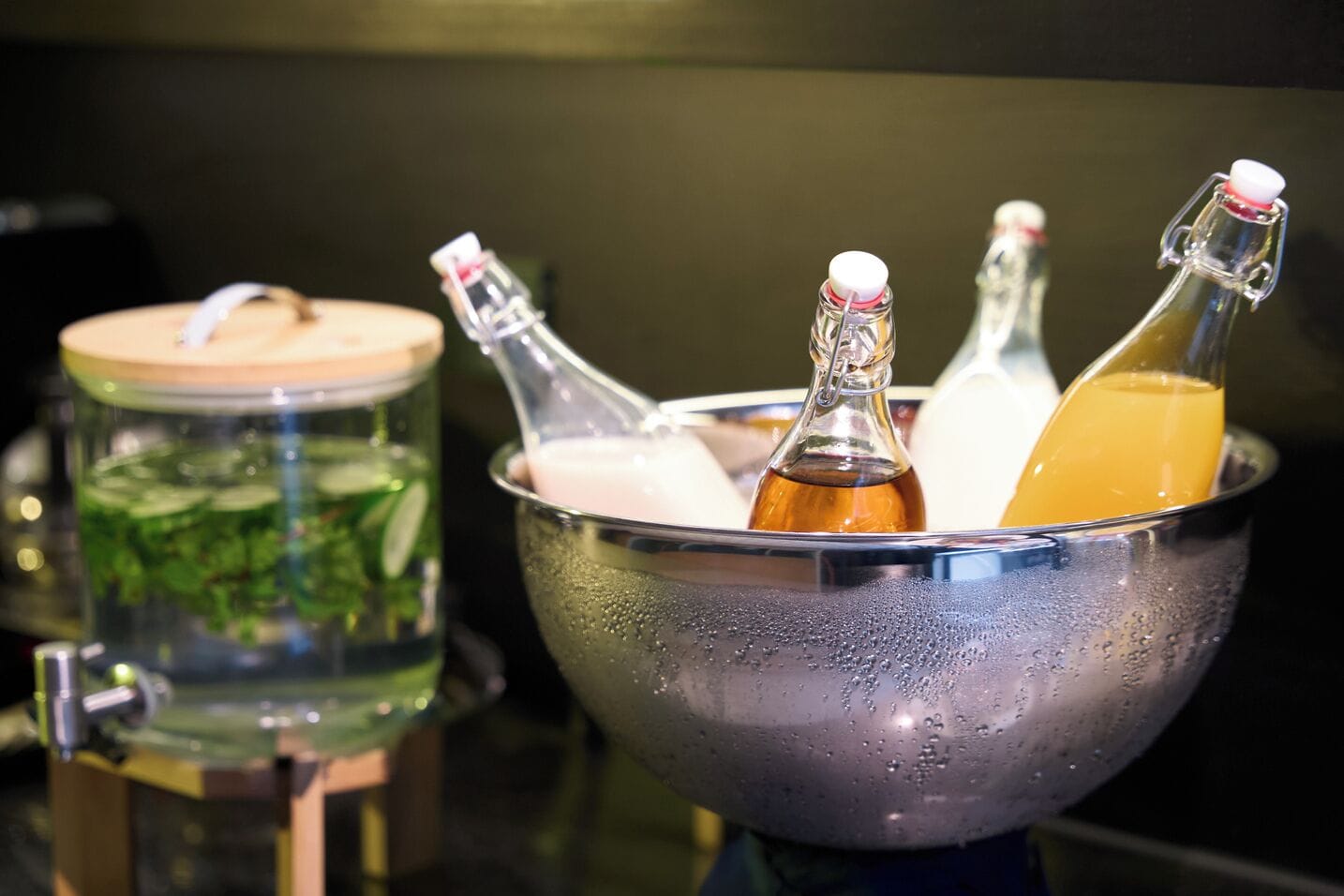 A metal bowl containing several bottles with liquids, a glass jar with a lid, and a metal container with a lid.