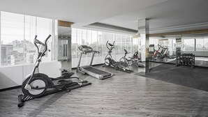 Un gimnasio moderno con diferentes máquinas de cardio, ventanas amplias y vista a la ciudad.