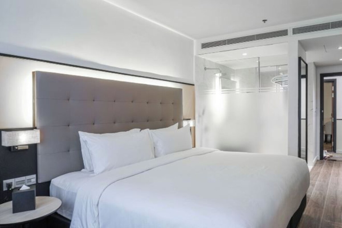 Une chambre d’hôtel moderne avec un grand lit, une table de chevet avec une lampe et une vue sur le couloir.