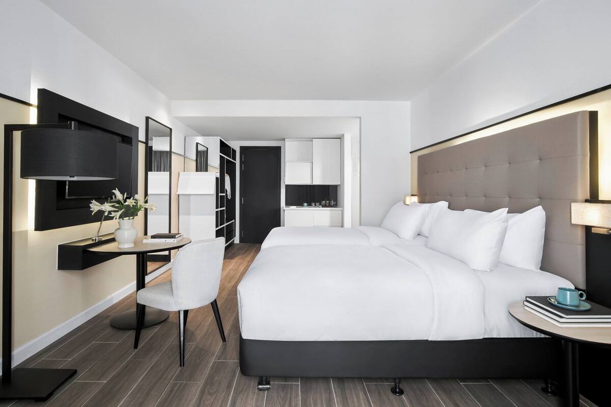 Une chambre d’hôtel moderne, dotée d’un grand lit, d’un bureau avec une chaise, d’une table de chevet avec une lampe et d’une armoire.