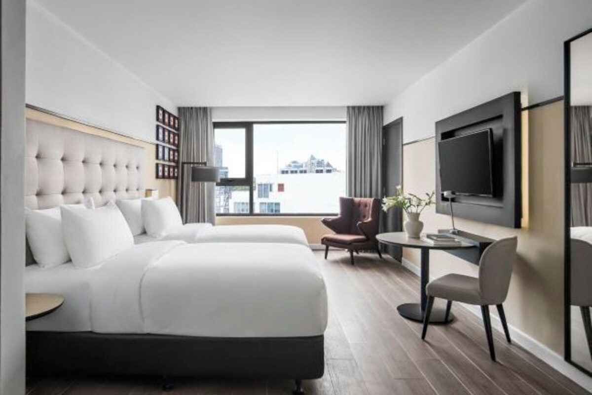 Une chambre d’hôtel moderne dotée d’un grand lit, d’un bureau, d’une chaise, d’une télévision et offrant une vue sur la ville.