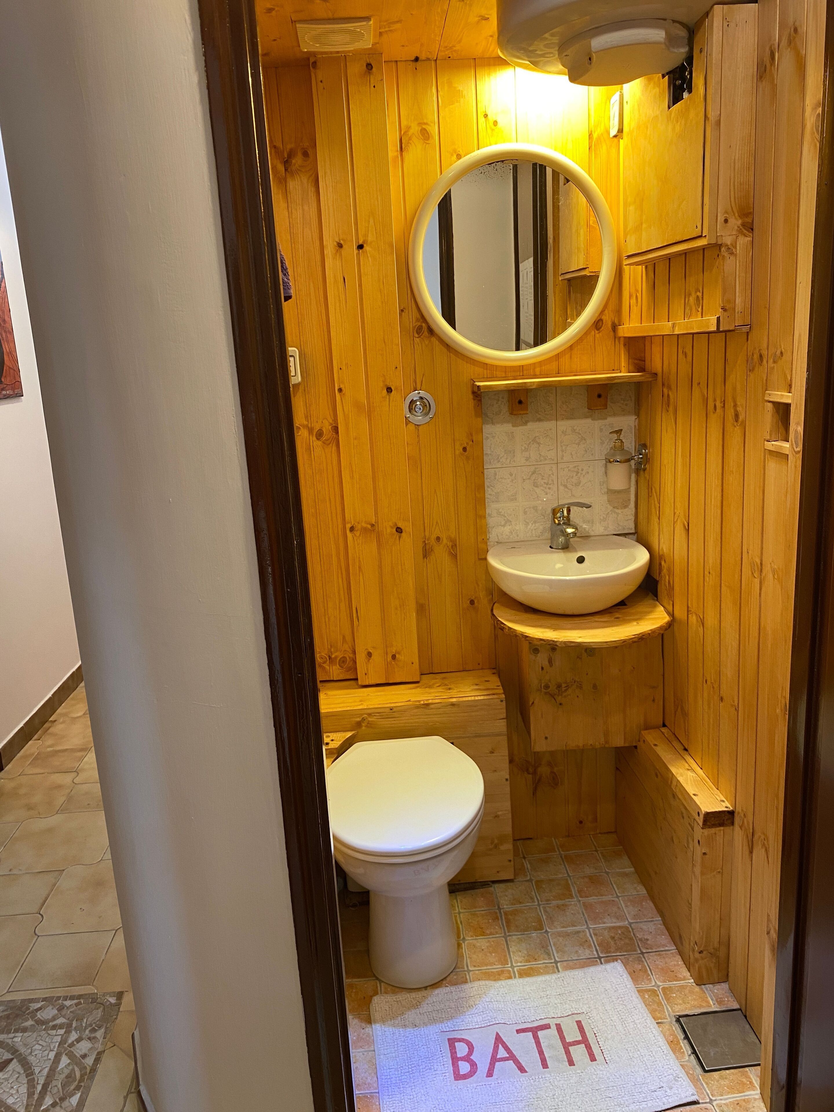 Een kleine houten badkamer met toilet, wastafel en spiegel.
