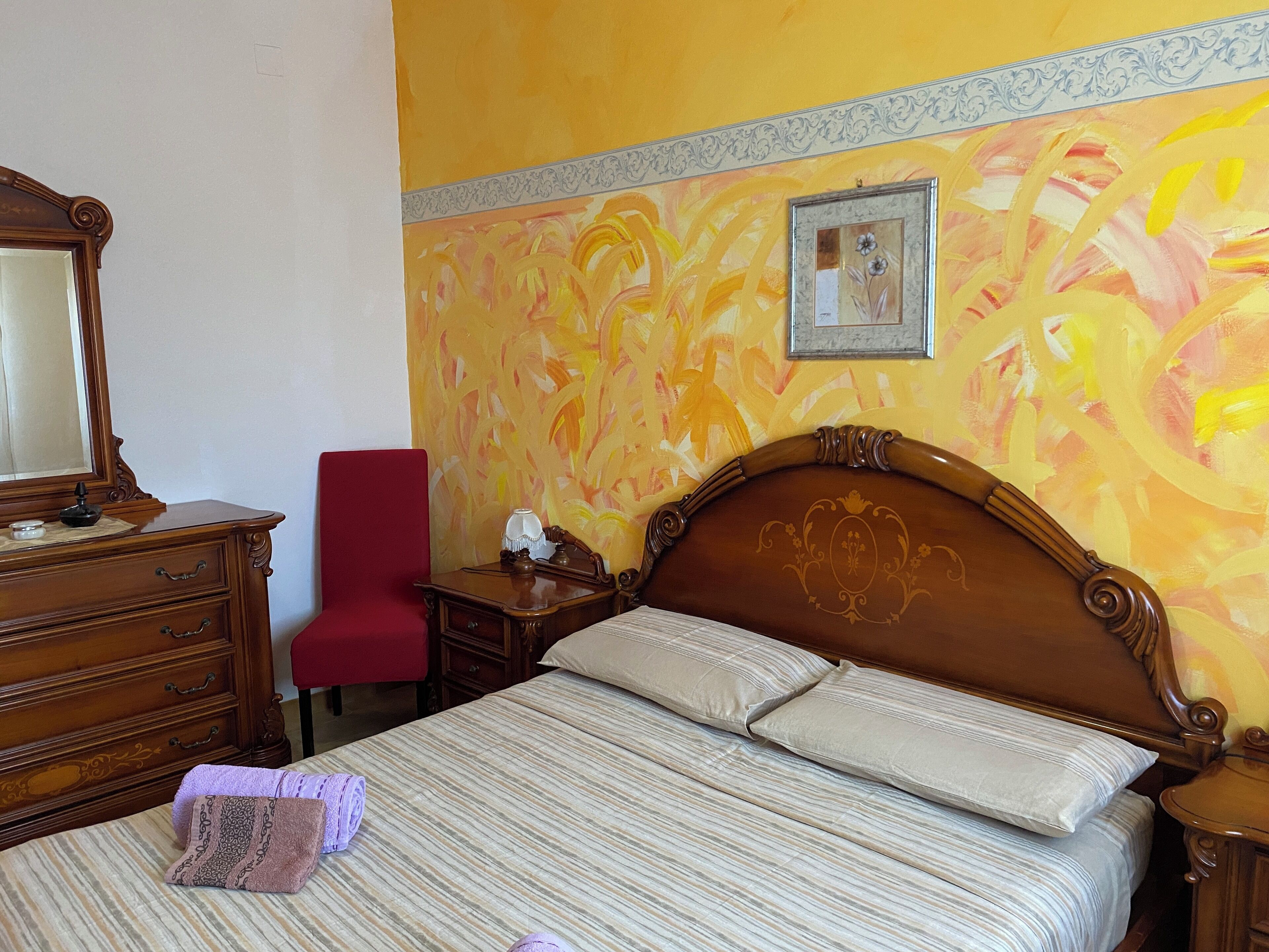 Ein Hotelzimmer mit einem hölzernen Bett, einem roten Sessel, einer Holzkommode und einem Spiegel.