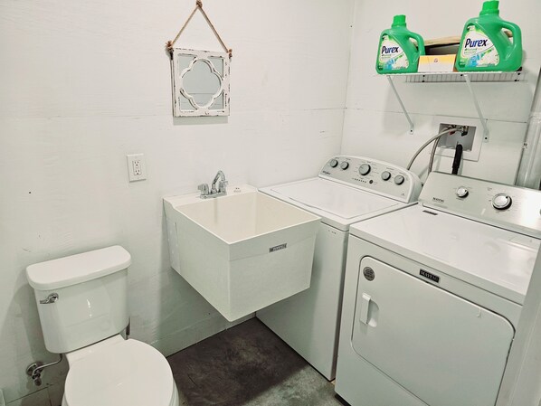 Une petite buanderie équipée d’un lave-linge, d’un sèche-linge, d’un évier et de toilettes.