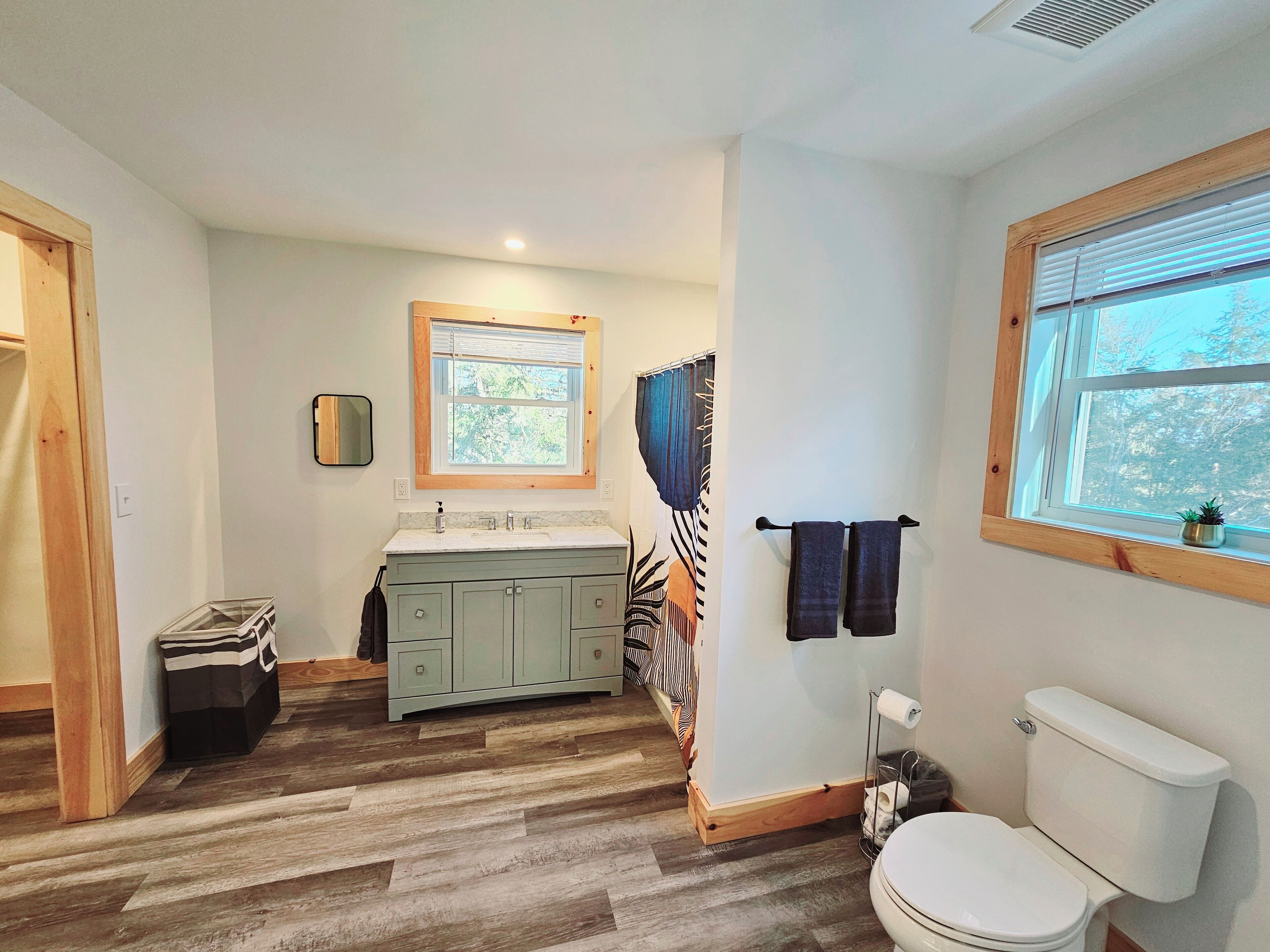 Une salle de bain avec un meuble-lavabo en bois, des toilettes, une fenêtre avec vue et un rideau de douche.