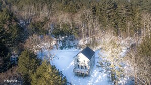 Une cabane entourée d’une forêt, le sol étant recouvert de neige.