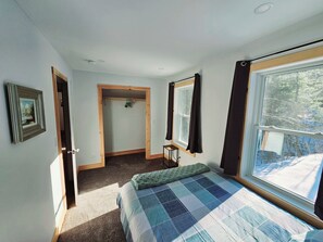 Une chambre à coucher avec un lit, une fenêtre avec des rideaux, une porte et une petite table.