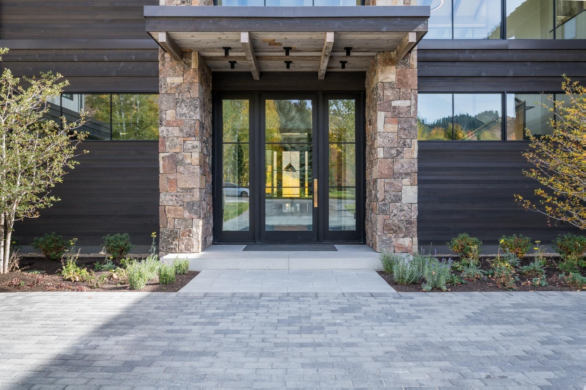 A modern building entrance with stone pillars, large glass doors, and a paved walkway.