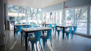 Un espacio interior amplio con varias mesas y sillas, ventanas grandes que dan a vistas de árboles, y un techo con paneles de madera.
