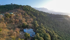 A two-story building with a flat roof, surrounded by dense forest and hills. - Acanti Dharamshala (Dharamshala)