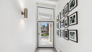 Un couloir avec une porte donnant sur un balcon, des murs blancs et une série de photographies encadrées accrochées au mur de droite.
