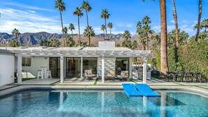 Une maison moderne avec une piscine, du mobilier de jardin et des palmiers.