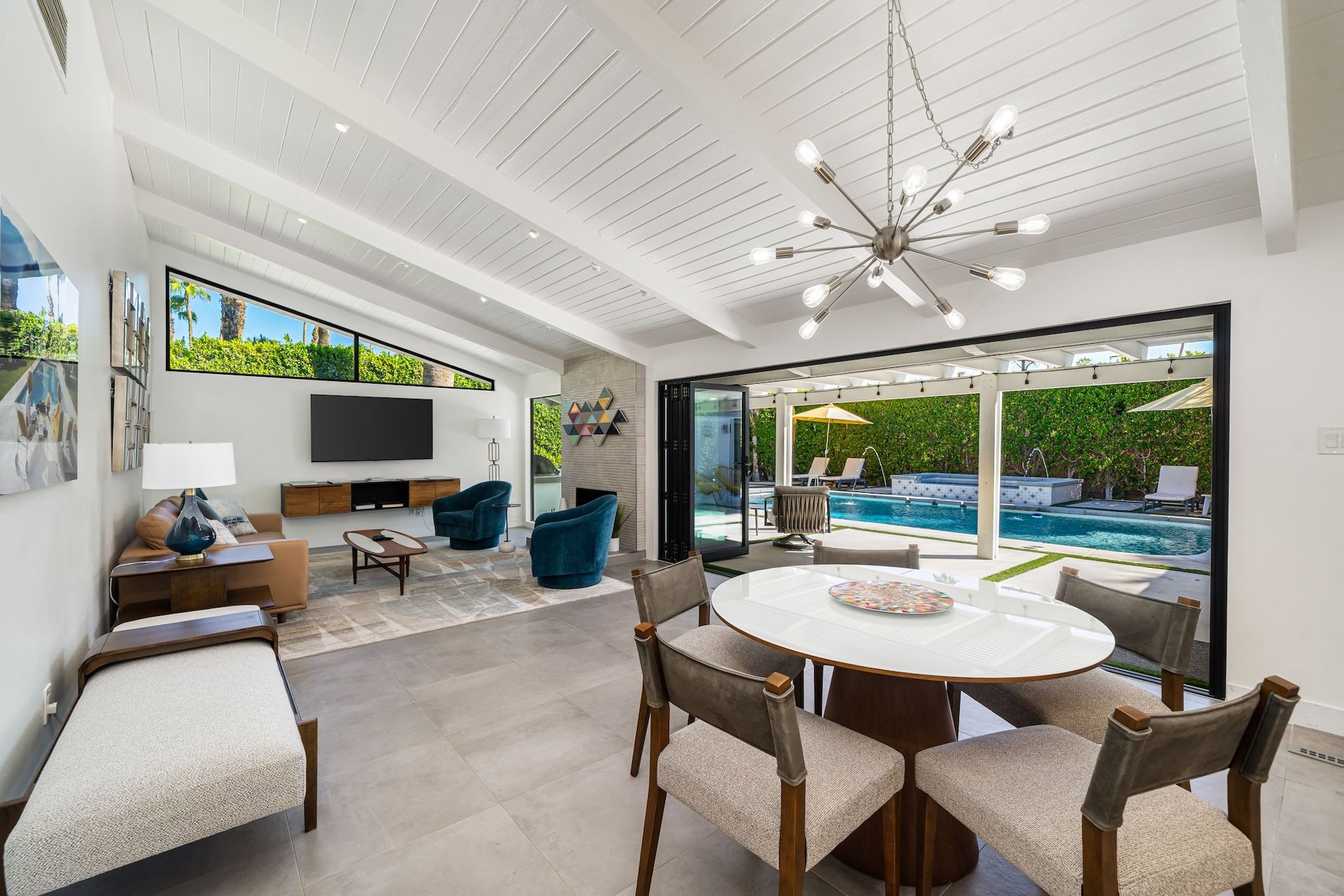 Step into your open-plan retreat where soaring vaulted ceilings meet mid-century flair. Relax in the living area or gather around the dining table, then slide open the doors to your private pool oasis framed by lush greenery.