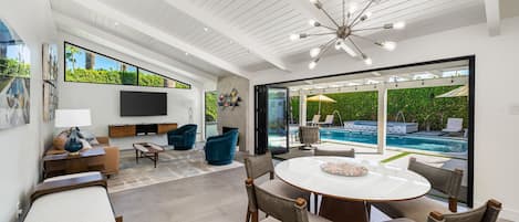 A modern living room with a pool view, a flat-screen TV, and a dining area.