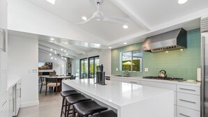 Une cuisine moderne dotée d’un grand îlot central, d’appareils électroménagers en acier inoxydable et d’un revêtement mural vert.