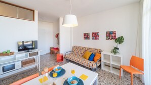 A modern living room with a television, sofa, dining table, and various decorative items. - Colorful beachfront apartment (Bibione)