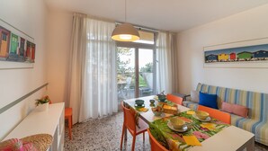 Ein Essbereich mit Tisch für zwei Personen, einer Couch und einem fensterbeprägten Bereich mit Vorhängen.