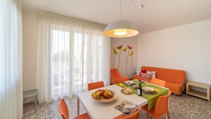 A dining area with a table set for two, a sofa, and a wall with floral artwork. - Large apartment with frontal sea view (Bibione)
