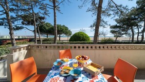 An outdoor dining area with a table set for breakfast, overlooking a beach and trees. - Large apartment with frontal sea view (Bibione)