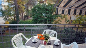 Un balcon avec une table dressée pour deux personnes, agrémentée d’un vase rempli de fleurs oranges, d’une théière, de tasses et d’une petite plante en pot.