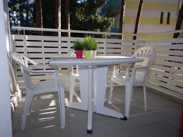 Un patio con una mesa blanca y dos sillas blancas, una planta en maceta y una valla blanca.