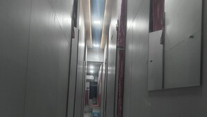 A narrow, well-lit hallway with mirrored walls and a tiled floor, leading to a room with a bed and a small table. - Green Apple PG & Dormitory (Mumbai)