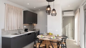 A modern kitchen with dark cabinets, a round dining table, and pendant lighting. - KS2 Exclusive Luxury Villa with 2 Bedrooms, Private Pool, BBQ &Outdoor Dining (Asprouliani)