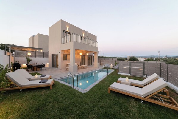 A modern two-story house with a swimming pool, outdoor seating, and a view of the landscape.