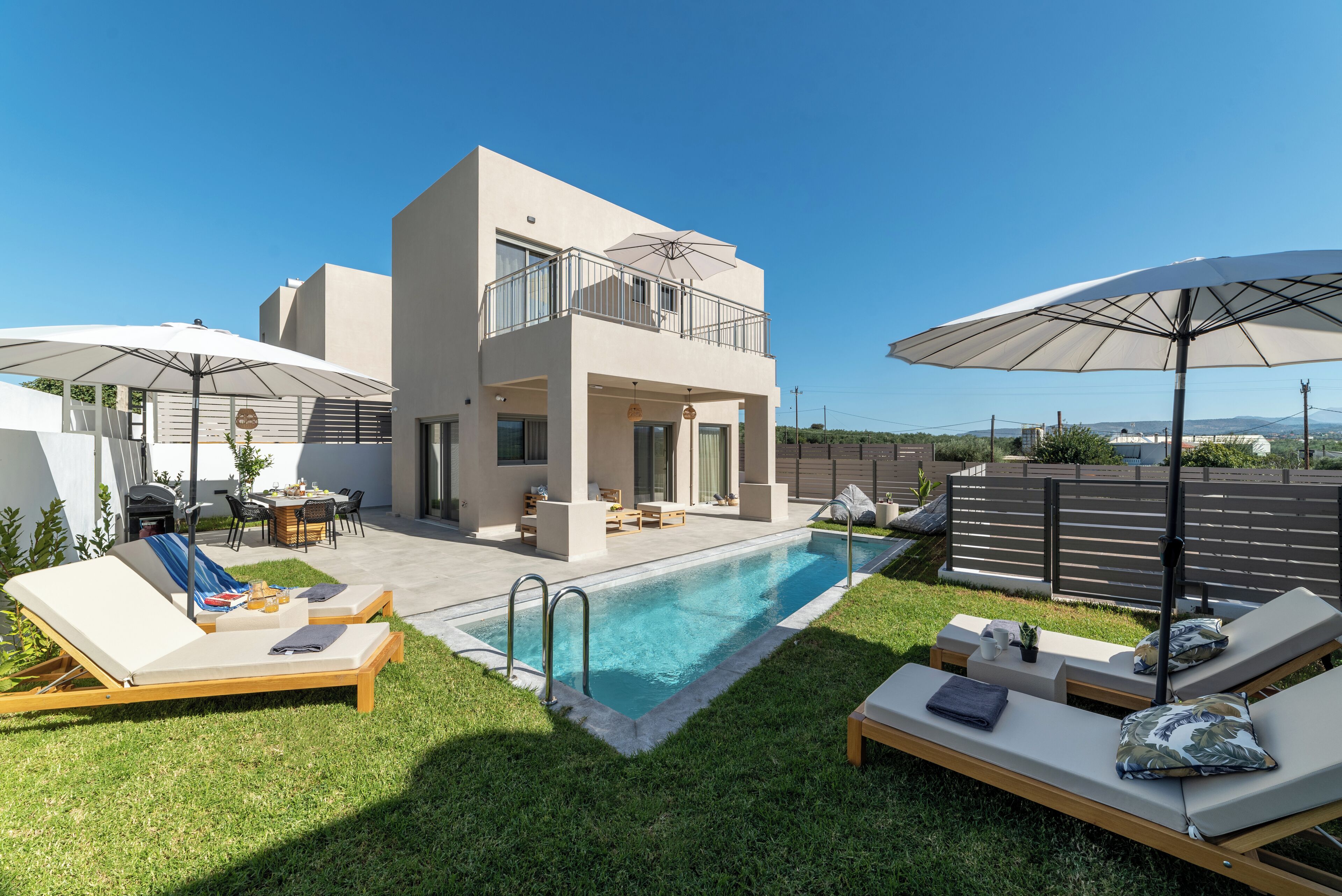 Een modern huis met twee verdiepingen, een zwembad, buiten zitplaatsen en parasols.