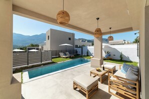 A modern outdoor pool area with lounge chairs, a wooden table, and a sofa.