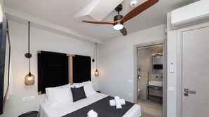 A modern hotel room with a large bed, a ceiling fan, a small round table, and a bathroom visible through an open door. - KS2 Exclusive Luxury Villa with 2 Bedrooms, Private Pool, BBQ &Outdoor Dining (Asprouliani)
