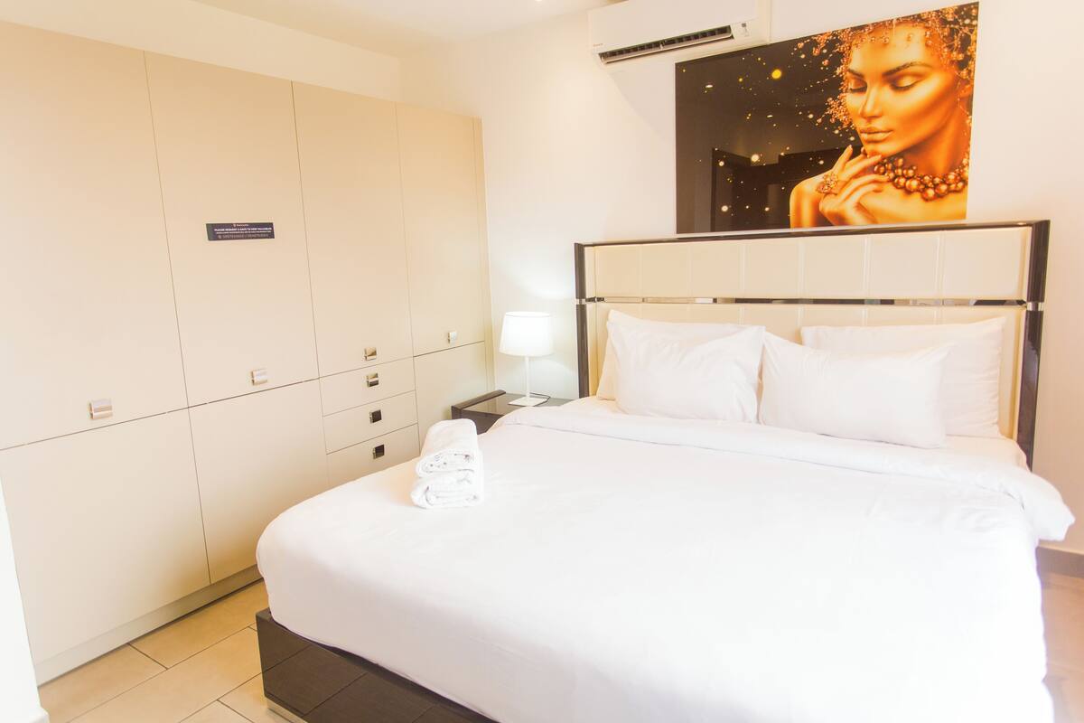 A hotel room with a large bed, a wardrobe, a nightstand, and a wall-mounted artwork.