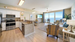 A modern kitchen with a sign reading "BEACH HOUSE," a dining area with a view, and a living room with a ceiling fan and a large window. - Sea and Ski: 1BR+ Bunk/2BA, Direct Gulf Views! Shores of Panama (Panama City Beach)
