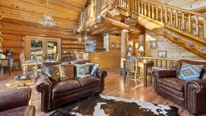A log cabin interior with a wooden staircase, leather furniture, and a cowhide rug. - Beaver Creek Luxury Lodge (Custer)