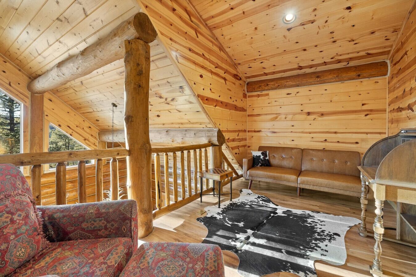 Interior de una cabaña de troncos con piso de madera, un sofá, un tapete estampado y un mantel de cuero de vaca.
