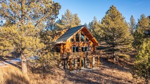 A wooden cabin with a balcony, surrounded by pine trees and dry grass. - Beaver Creek Luxury Lodge (Custer)