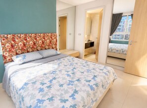 A hotel room with a bed, a bathroom, and a view of buildings through the window. - GSR - Grande Caribbean (Pattaya)