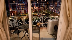 A balcony with a table and chairs, a small heater, and a view of a building with multiple balconies at night. - GSR - Grande Caribbean (Pattaya)
