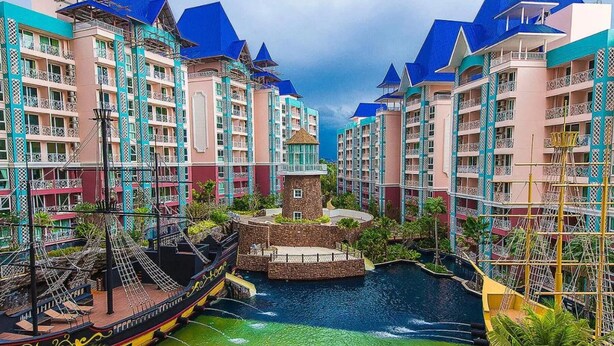 A resort with multiple high-rise buildings, a central water feature, and a boat docked by the water. - GSR - Grande Caribbean (Pattaya)