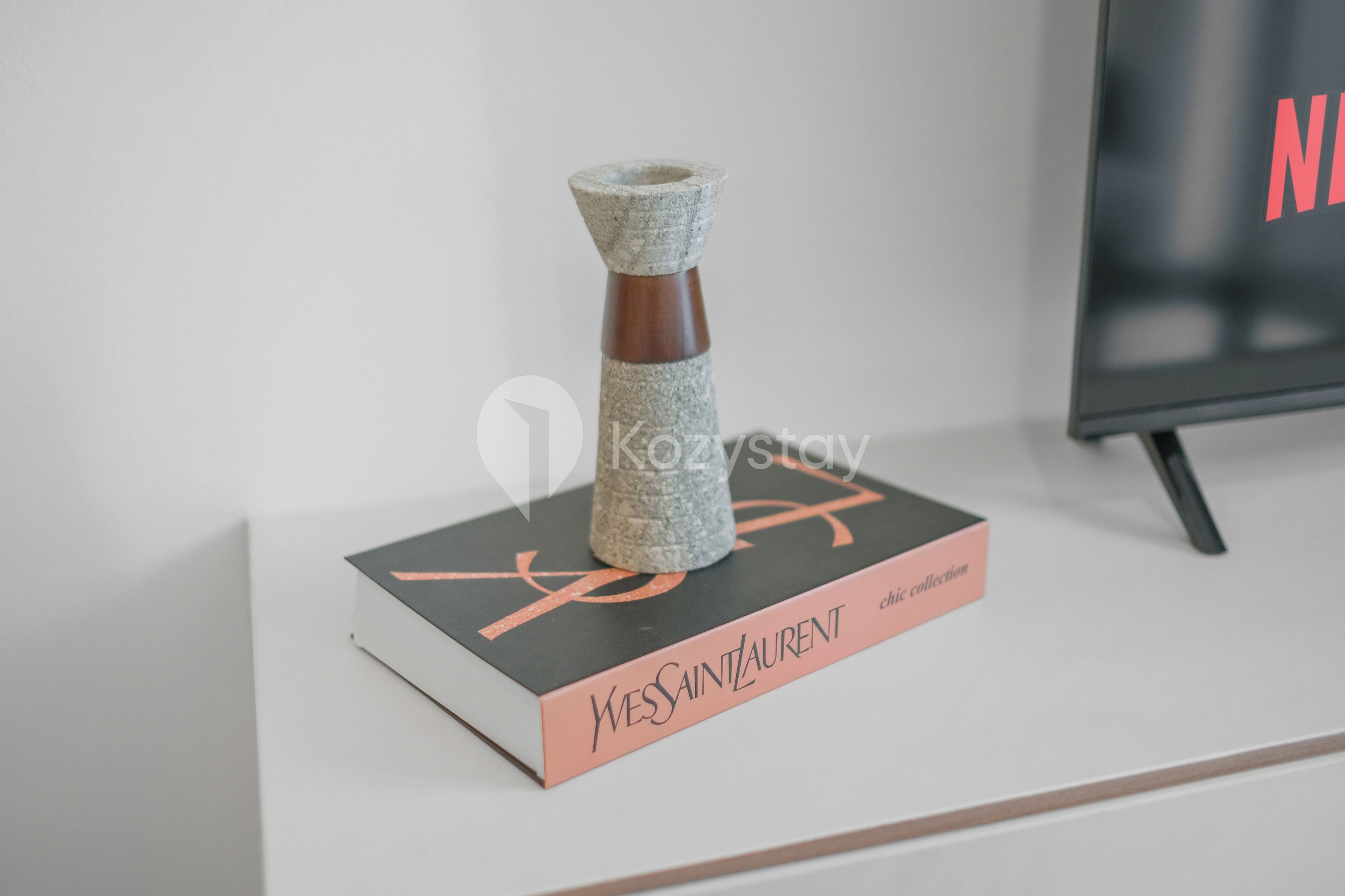 A book titled 'Yves Saint Laurent chic collection' with a stone vase on top, placed on a white surface.