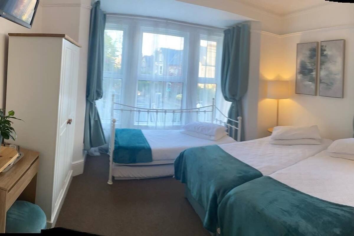 A hotel room with two beds, a desk, a chair, a lamp, and a window with curtains.
