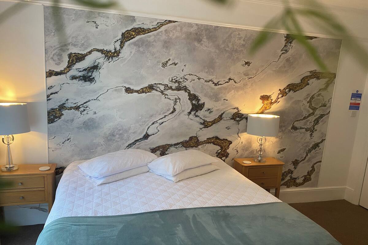 A hotel room with a bed, two bedside tables, and a marble-patterned wall.