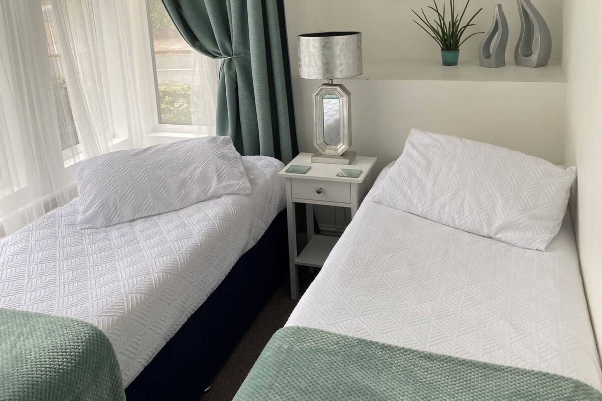 A hotel room with two beds, a nightstand, a lamp, a framed picture, and a window with curtains.