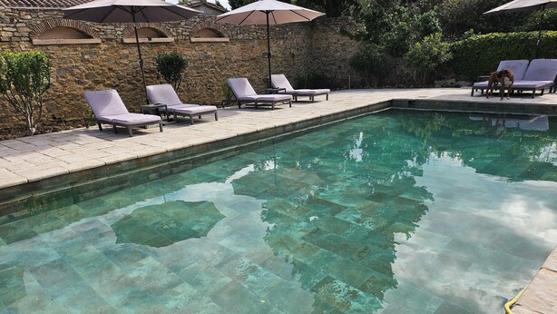 Una piscina cristalina con piso de baldosas, rodeada de sillones de descanso y sombrillas.