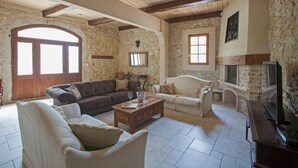 Un salón comedor espacioso con paredes de piedra, vigas de madera, una chimenea y un amplio ventanal de arco.
