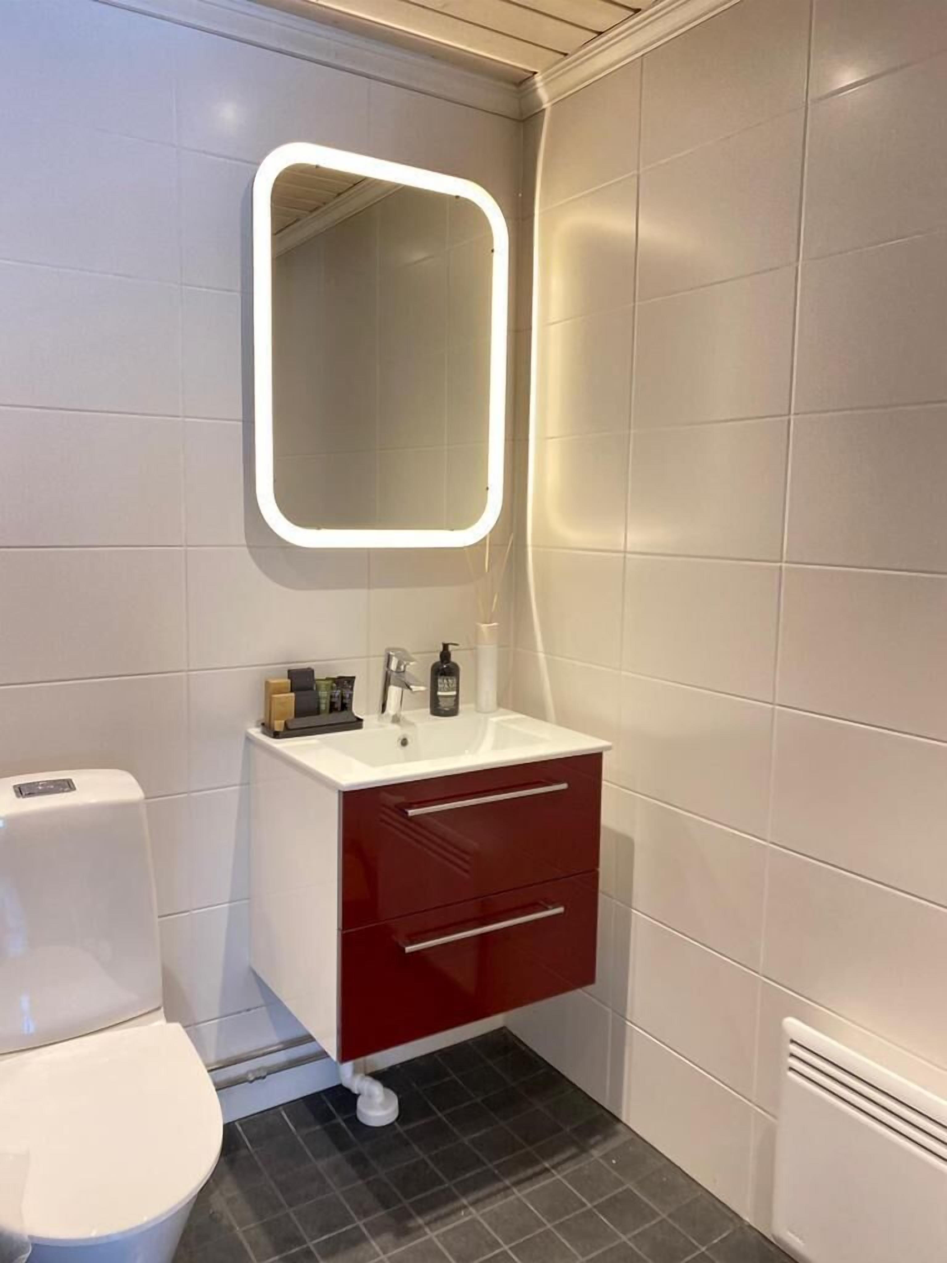 A modern bathroom with a white toilet, a red vanity with a mirror, and a white sink.