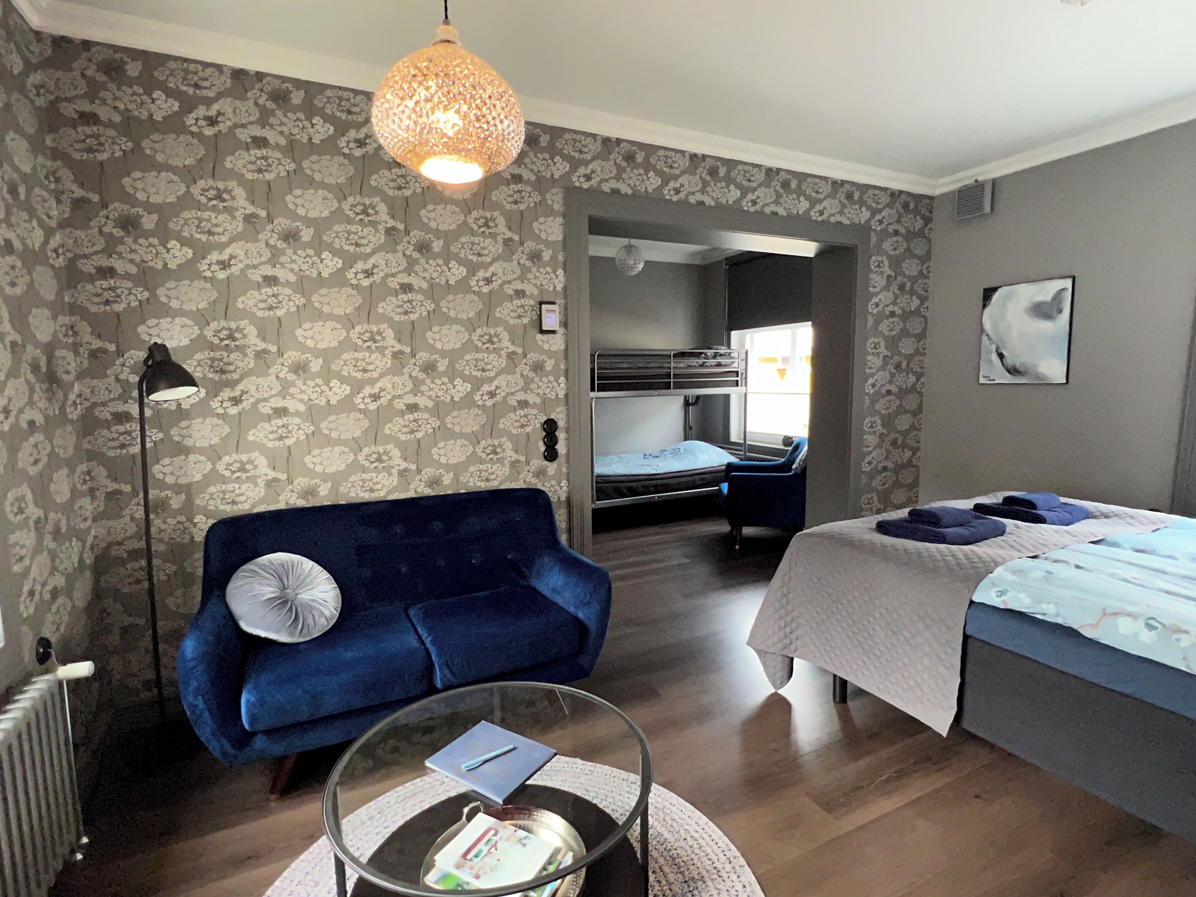 Une pièce avec un canapé bleu, un lit recouvert d’une couette blanche, un luminaire suspendu et un radiateur.