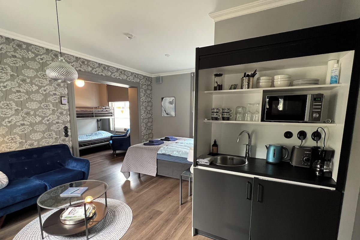 A compact hotel room with a kitchenette, a sofa, a coffee table, and a bed.
