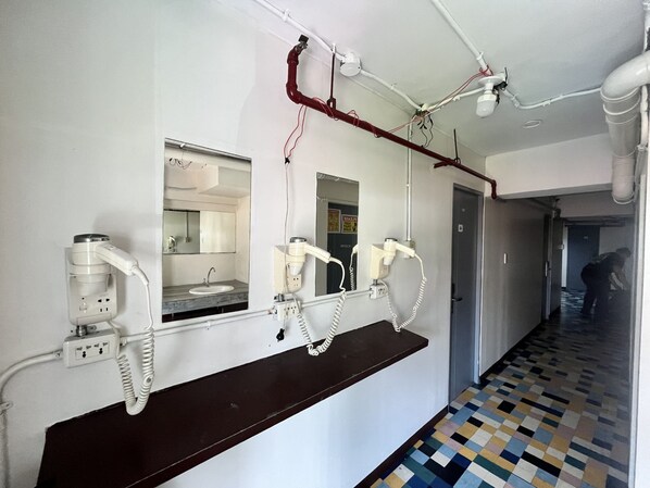 A hallway with a mirror, a sink, and hair dryers mounted on the wall.